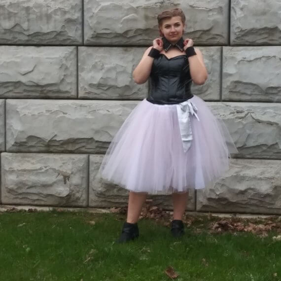 Black pleather sweetheart corset with midi length pink tulle skirt styled with black ankle boots, a silver silk sash, an upcycled black shirt collar necklace, and upcycled wrist cuffs. Model Alexis Remington is grabbing the collar