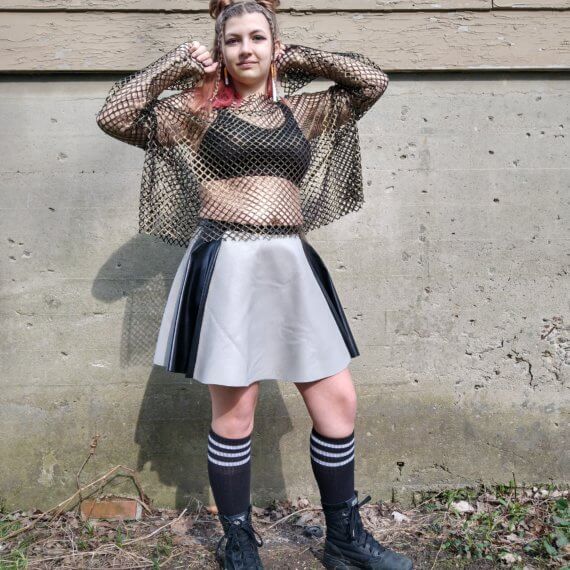 Gold long sleeve fishnet oversized top paired with a grey leather skirt with two black leather stripes down each side. Styled with knee high black socks and army combat boots and fake cigarette earrings