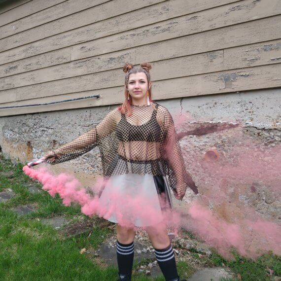 Gold long sleeve fishnet oversized top paired with a grey leather skirt with two black leather stripes down each side. Styled with knee high black socks and army combat boots and fake cigarette earrings