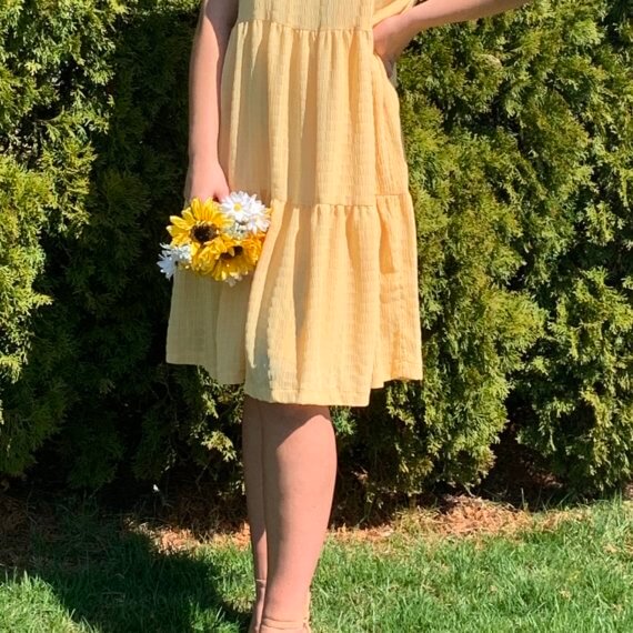 Sleeveless golden yellow trapeze knee-length dress with high halter neckline, and sunflower accent.