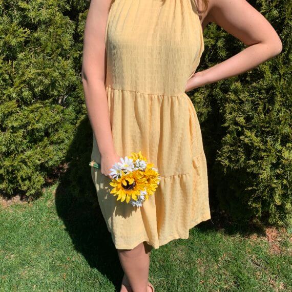 Sleeveless golden yellow trapeze knee-length dress with high halter neckline, and sunflower accent.