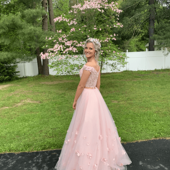 A-line off the shoulder short sleeve gown with a lace designed bust and pink fabric with lace flowers along the bottom half of the gown.