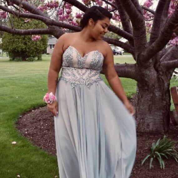 A-line sweetheart prom gown with pink and silver fabric. The bust of the gown is covered in silver crystals and gems. The right side of the gown also has a slit. The back of the down has a soft pink ribbon through the corset of the gown.