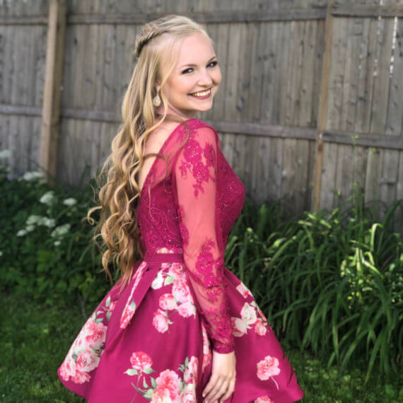 Magenta above the knee prom dress. Floral fabric along wit floral lace on the sleeves and bust of the dress. With a low back.