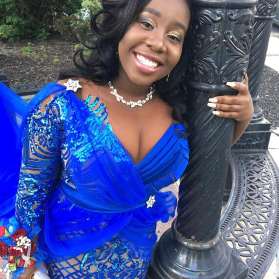 Fitted long sleeve blue prom gown with a v neckline. The gown has a slit up the front of the gown. The sleeves and bottom half of the dress are lace fabric both blue and nude. This gown was handmade by her father.