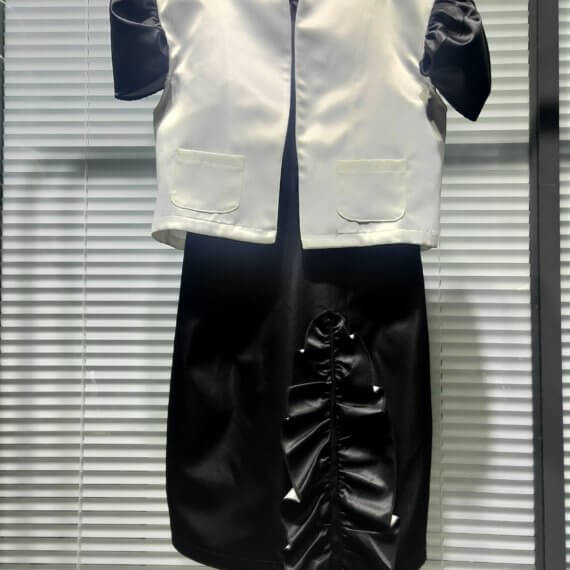 A two piece look of a black satin sleeveless shift dress with a mandarin collar and asymmetrical vertical ruffle on the skirt paired with a bolero length white satin jacket with contrasting black, set in, puff, cap short sleeves. The jacket has a stand up shawl collar