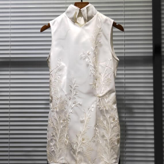 White silk satin shift dress with white floral embroidered overlay. It is sleeveless s with a mandarin collar. This mid thigh length dress has a band of black tulle around the hem.
