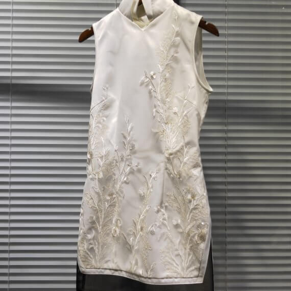 White silk satin shift dress with white floral embroidered overlay. It is sleeveless s with a mandarin collar. This mid thigh length dress has a band of black tulle around the hem.