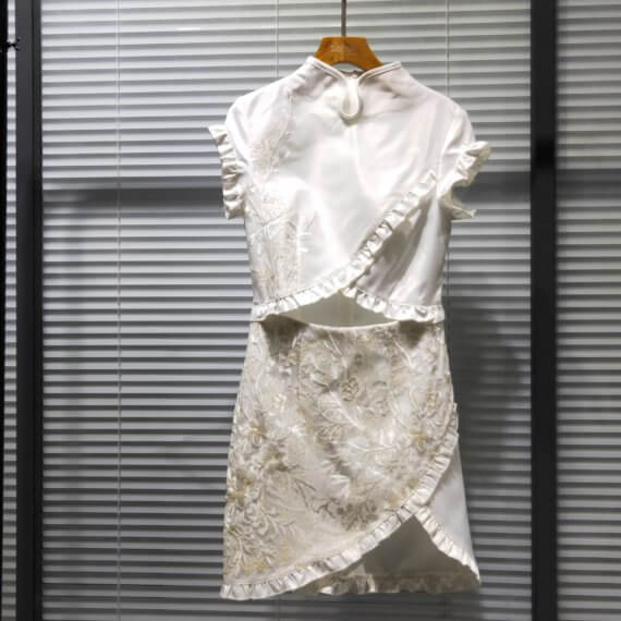 White silk satin mid thigh length short sleeve dress with white floral embroidere d overlay. Bodice and skirt crossover style results in a triangular exposed midriff. Also, cross over edges of bodice and skirt are finished with a ruffle.