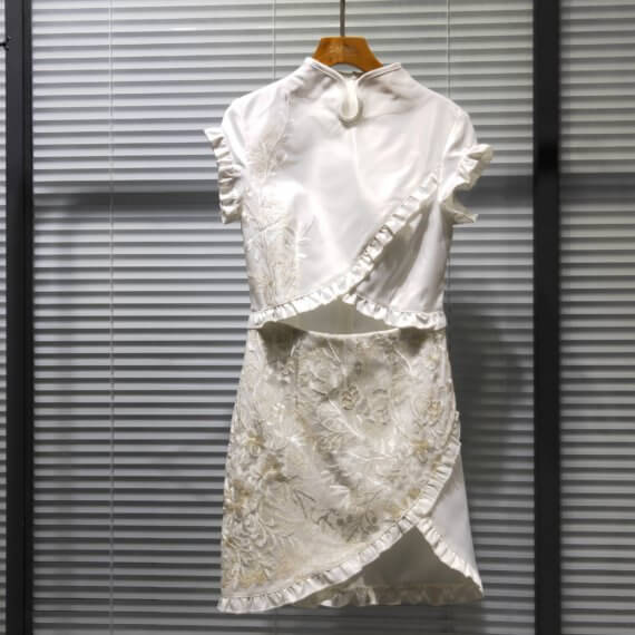 White silk satin mid thigh length short sleeve dress with white floral embroidere d overlay. Bodice and skirt crossover style results in a triangular exposed midriff. Also, cross over edges of bodice and skirt are finished with a ruffle.